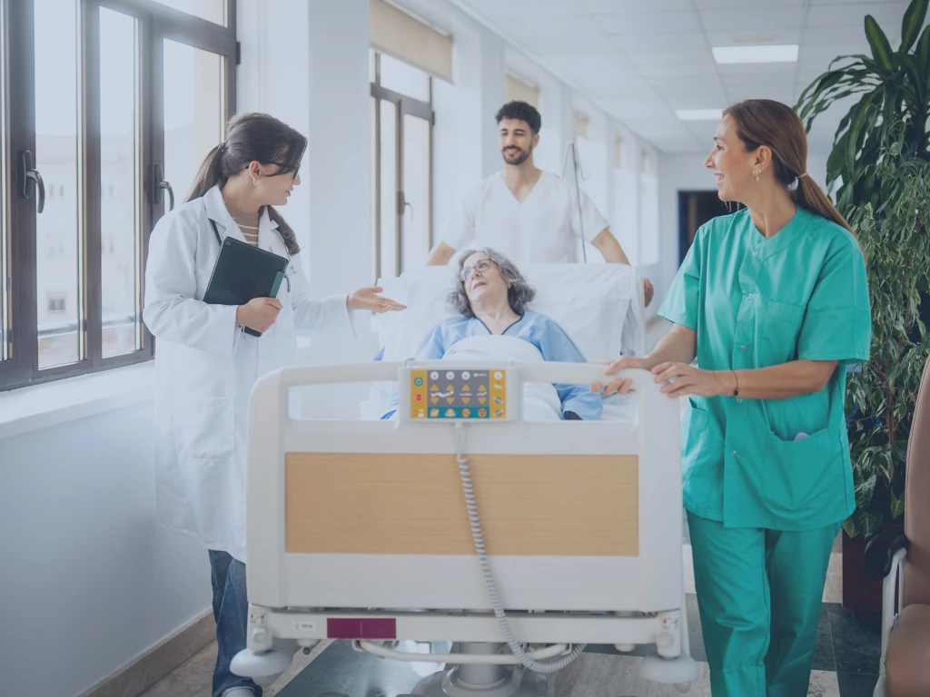 Blick auf das Gesundheitssystem der Zukunft Eine Ärztin und zwei Pflegekräfte schieben das Bett einer Patientin und besprechen sich dabei mit ihr.