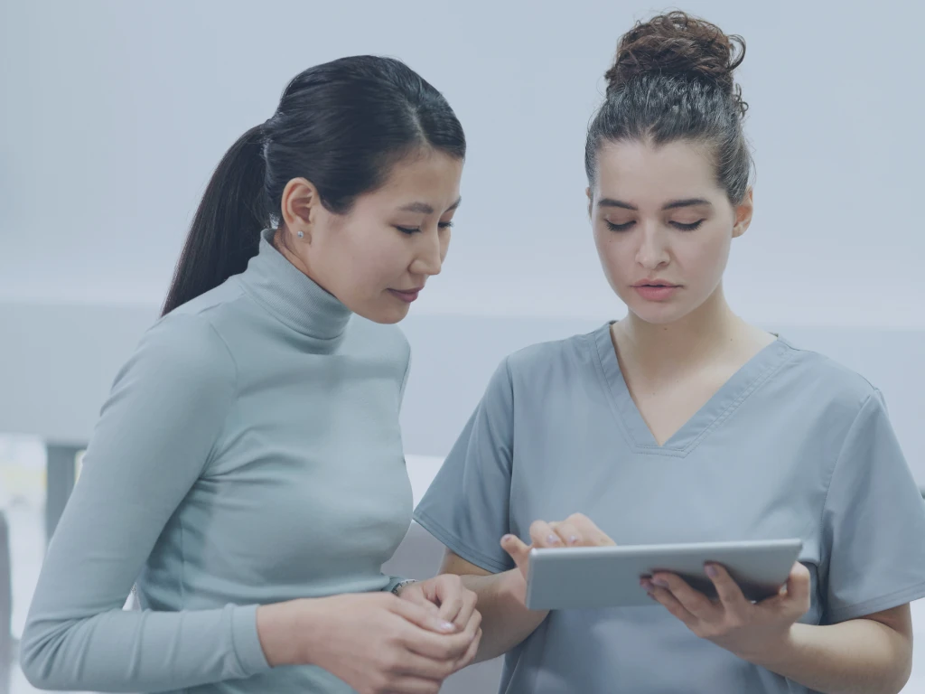 Digitale Reifegradmessung Eine Pflegerin spricht mit einer Patientin und blickt dabei auf ihr Pad, auf dem sie das Patientenportal nutzt.