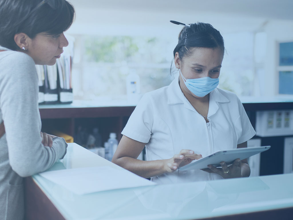 Persönlicher Kontakt in der Patientenaufnahme Eine Mitarbeitende und eine Patienten tauschen sich über Daten in der Anmeldung aus.