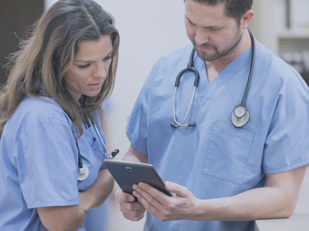 Zwei Pflegekräfte betrachten Informationen zu einem Patienten auf einem Pad, um ein perfektes Verweildauermanagement zu erreichen.