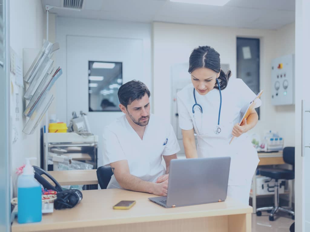 Zwei Ärzte nutzen das POLAVIS Patientenportal auf einem Laptop. Sie stehen nebeneinander im Stationszimmer.