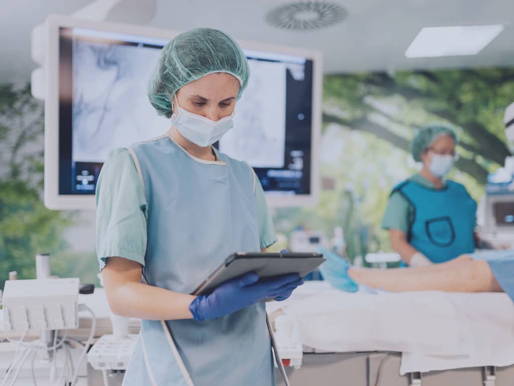 Eine Ärztin steht im Operationssaal und betrachtet Patientendaten im POLAVIS Patientenportal.